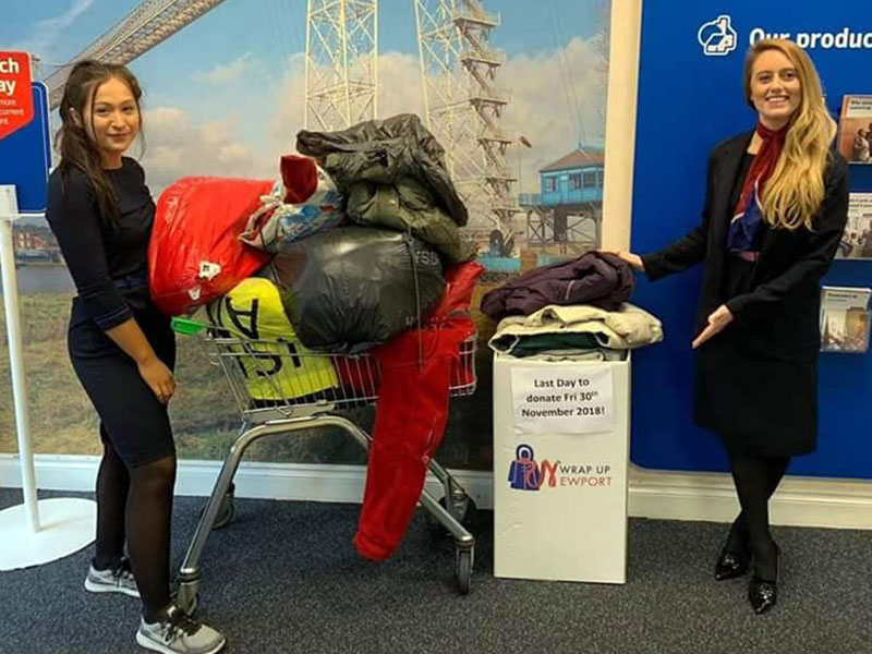 two women pose with a trolly filled with donated coats for Wrap Up Newport