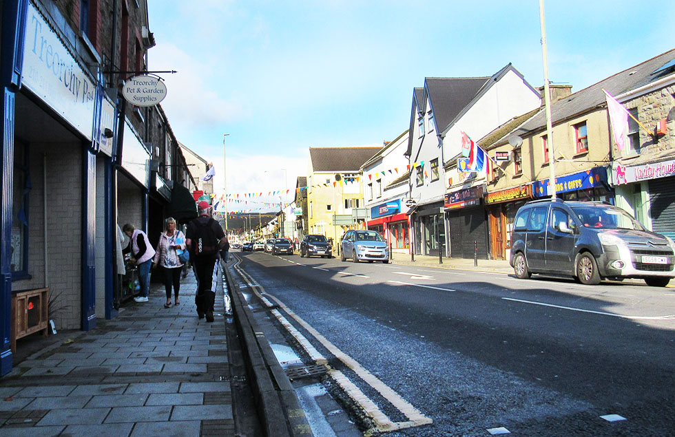 Treorchy high Street on a Saturday, showing shoppers and shop fronts, and flags and bunting