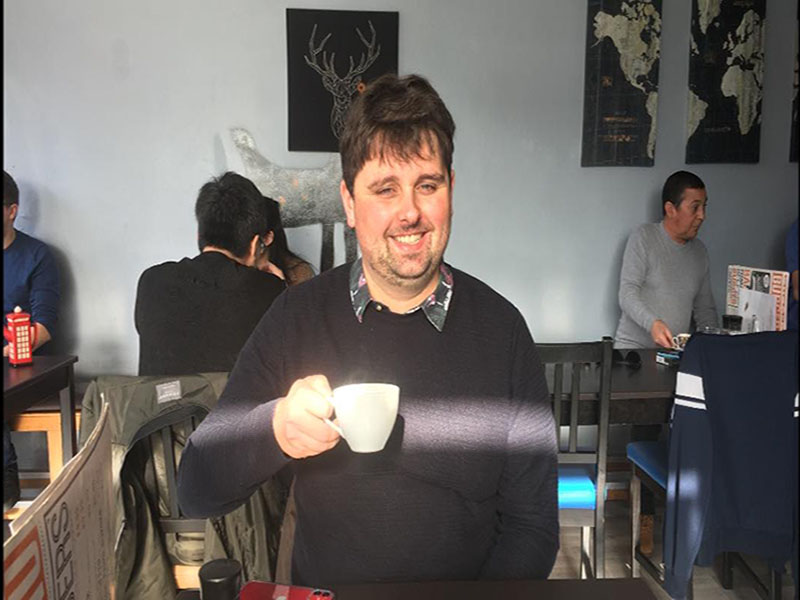 Jack Mac drinking coffee in a local cafe with a grin