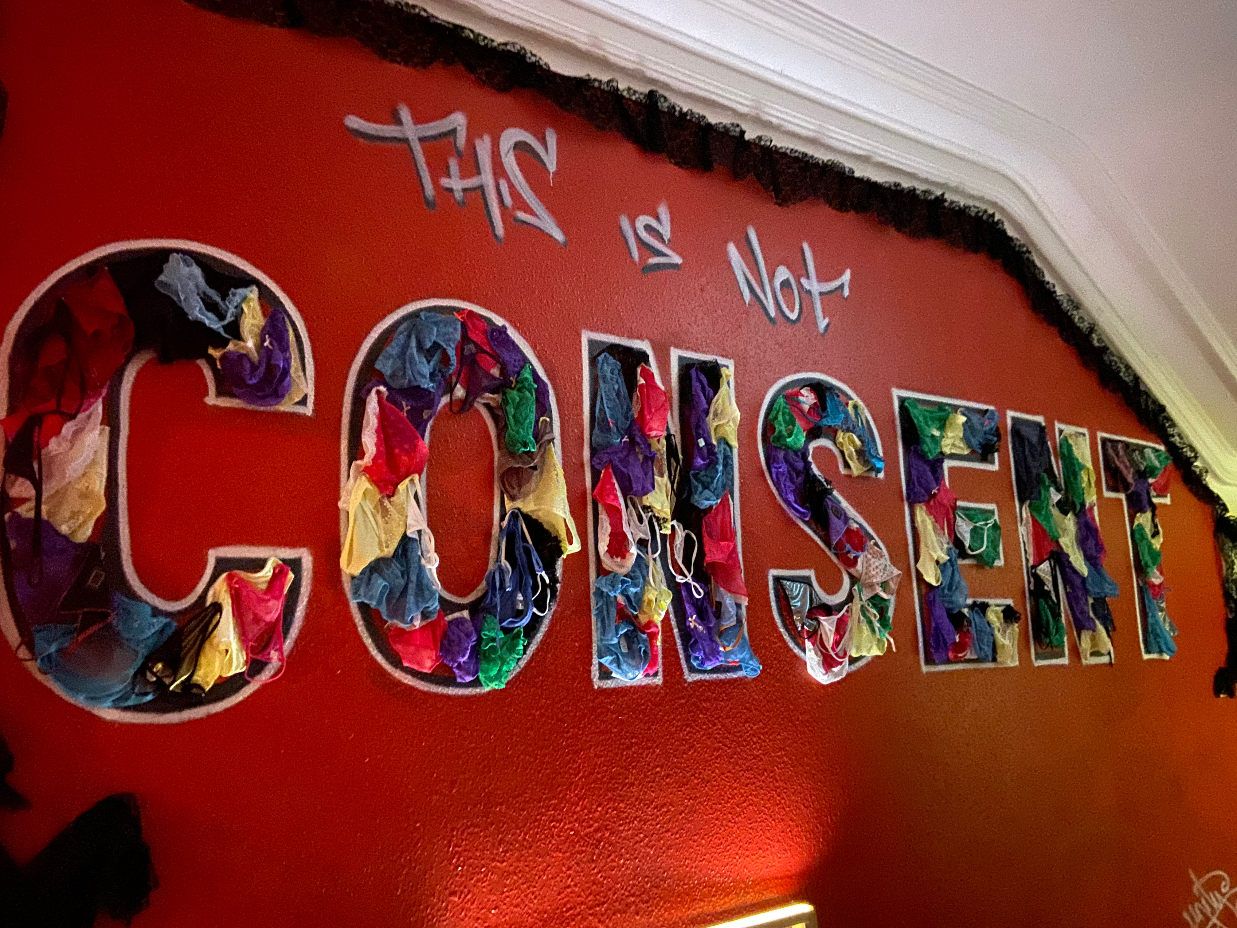 Women's underwear is pinned on the wall to fill in the word consent, in the phrase "this is not consent"