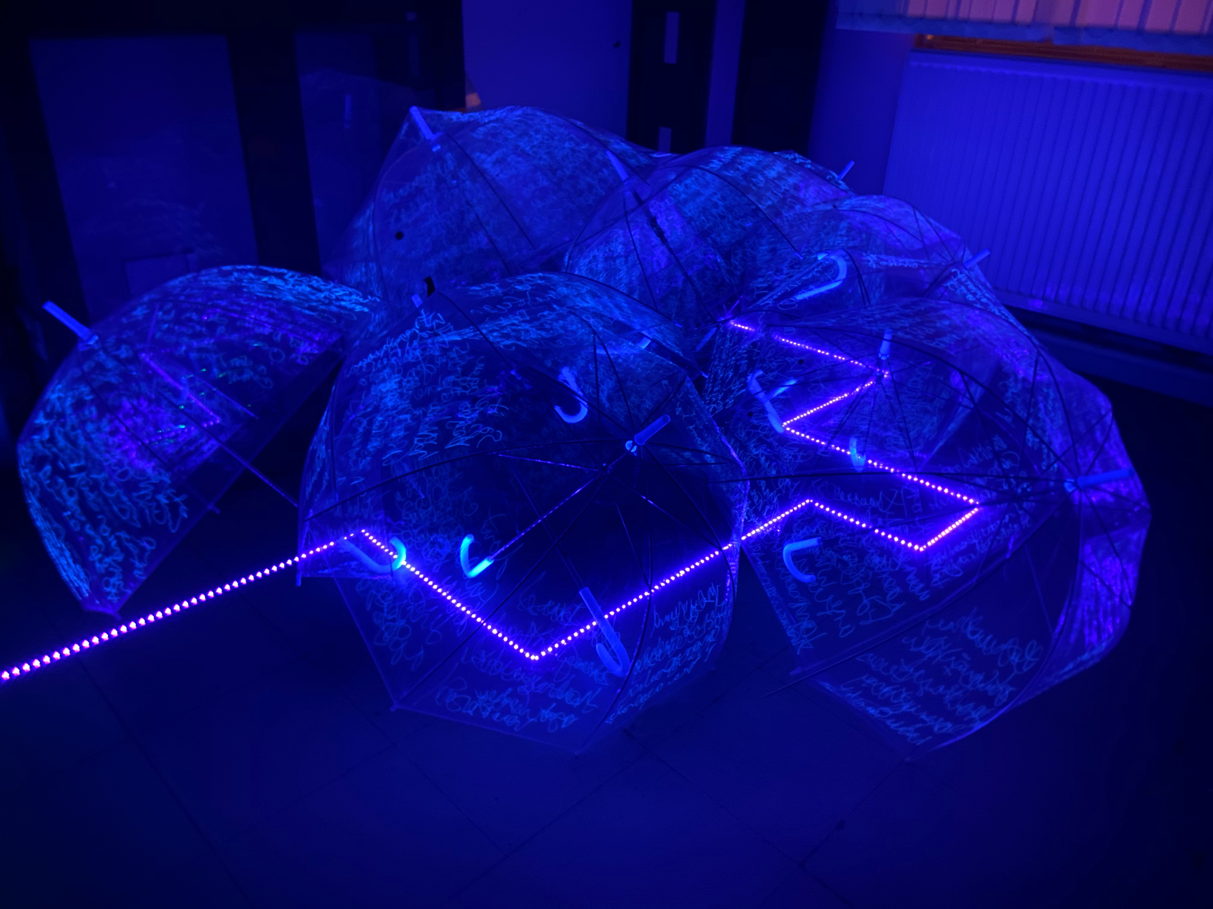 A strip of neon blue lights runs along the floor, covered by transparent plastic umbrellas with neon scrawls on them