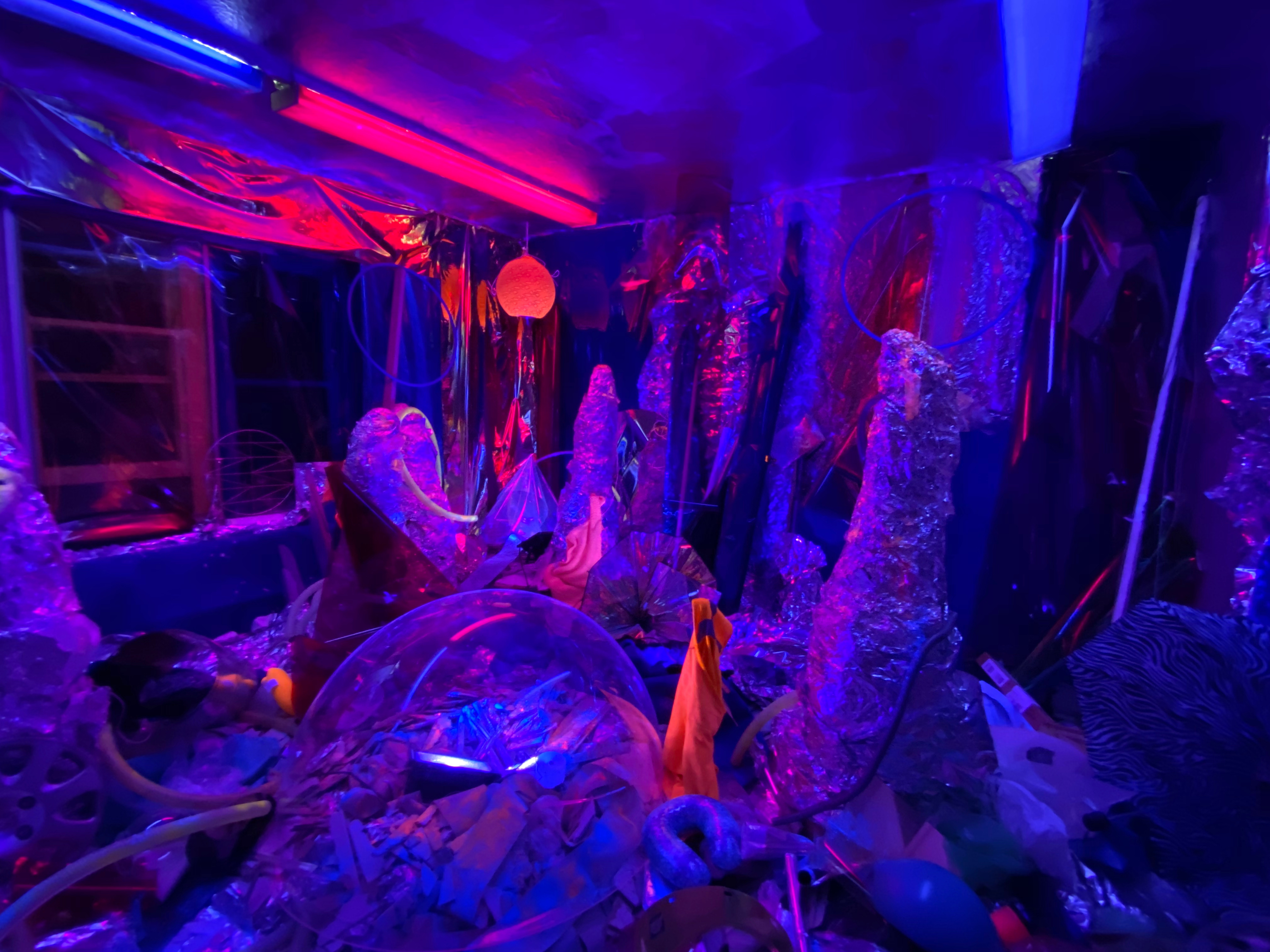 Tinfoil and clear orbs fill the room in a space-esque layout, illuminated by blue and red lights