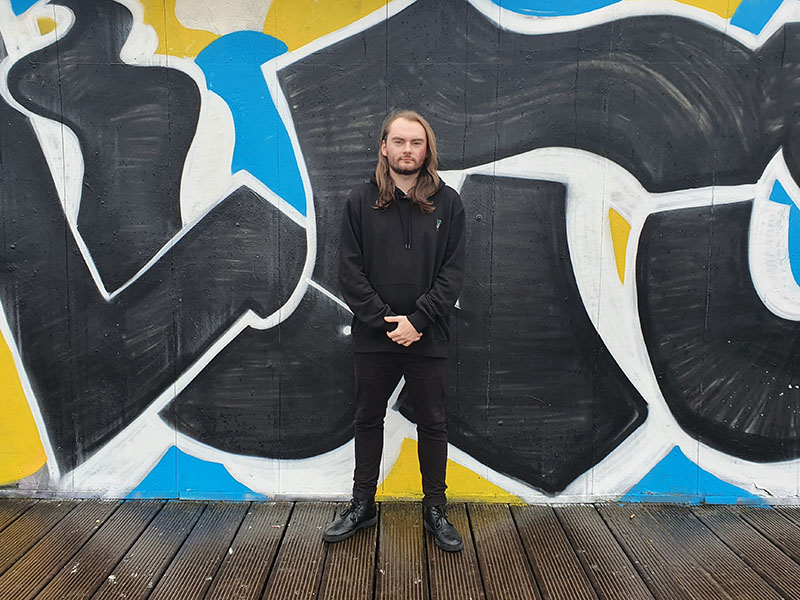 A photo of Morgan Richards of Sappenin' Podcast standing against a colourful graffiti wall in Cardiff.