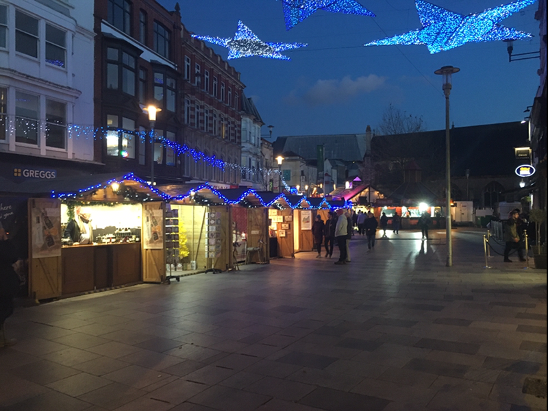 The Christmas lights over Cardiff market and people looking at the stalls.