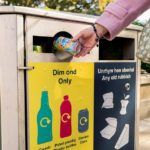 someone putting a plastic bottle in a yellow recycling bin