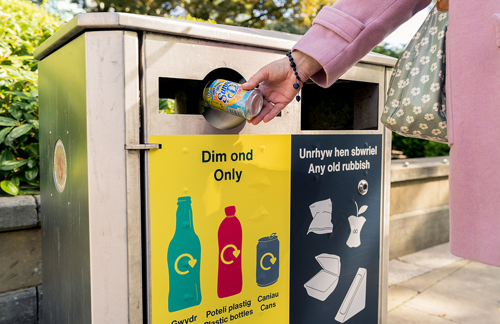 someone putting a plastic bottle in a yellow recycling bin