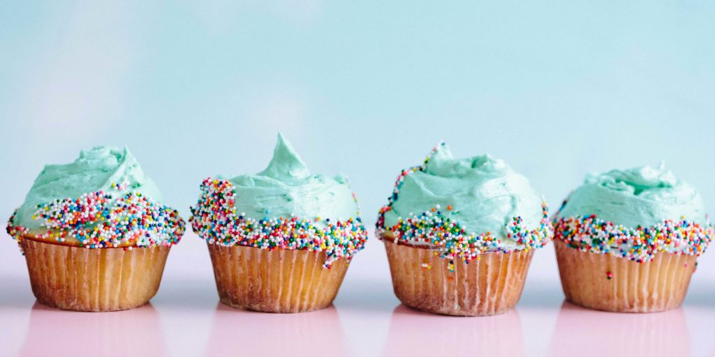 Four cupcakes with blue icing and sprinkles