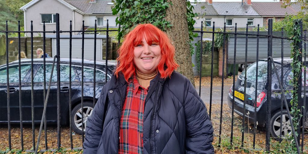 Non-binary body positivity Instagrammer Dot Masters with bright red hair smiles at the camera, with trees behind them