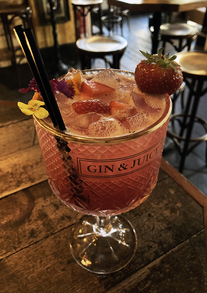 A pink coloured non-alcoholic drink in a large cocktail glass, garnished with ice, flowers and a strawberry.