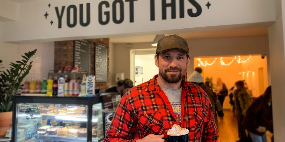 Founder, Ian Brodie, is holding a cup of hot chocolate popular amongst the homeless. There's a sign saying 'You got this' in the background at Bricks & Mortar