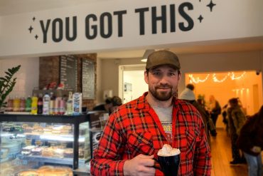 Founder, Ian Brodie, is holding a cup of hot chocolate popular amongst the homeless. There's a sign saying 'You got this' in the background at Bricks & Mortar