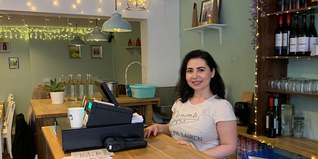 Vegan business owner smiles behind the decorated bar of her restaurant