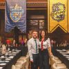 A man and a woman dressed up in Slytherin and Gryffindor uniforms, standing in front of the Hogwarts house banners in Coal Exchange Hotel