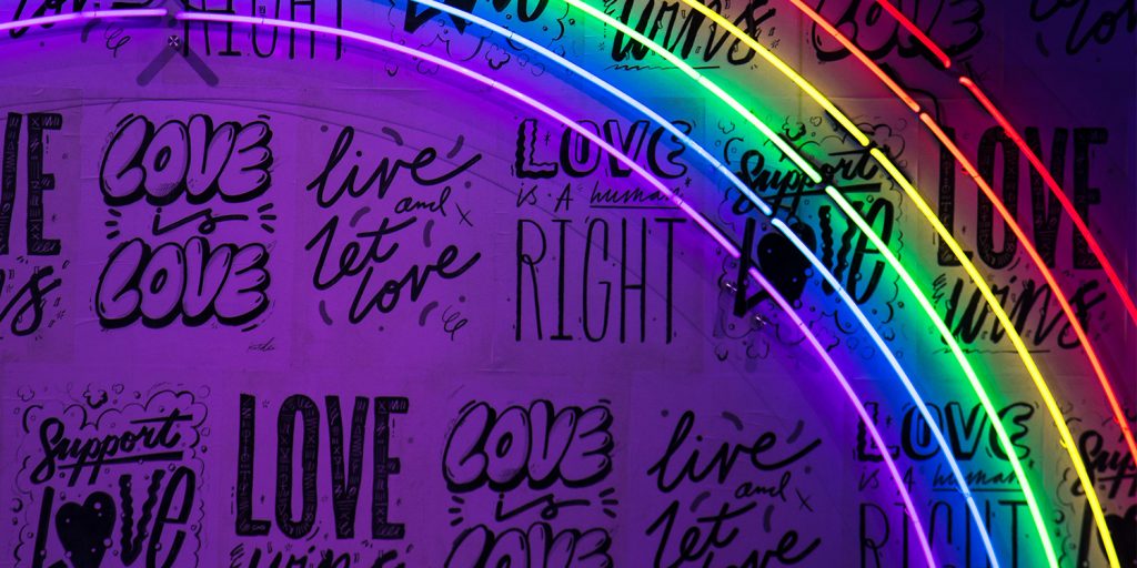 A wall with variations of "love wins" scribbled all over, with a rainbow light, to shed light on homophobia against POCs