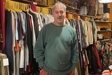 The picture shows a vintage clothing shop owner in his store