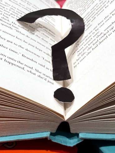 An open book with a black paper question mark in the middle.