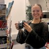 Young female photographer holds camera infant of bookshelf as she joins the creative industry in Cardiff.