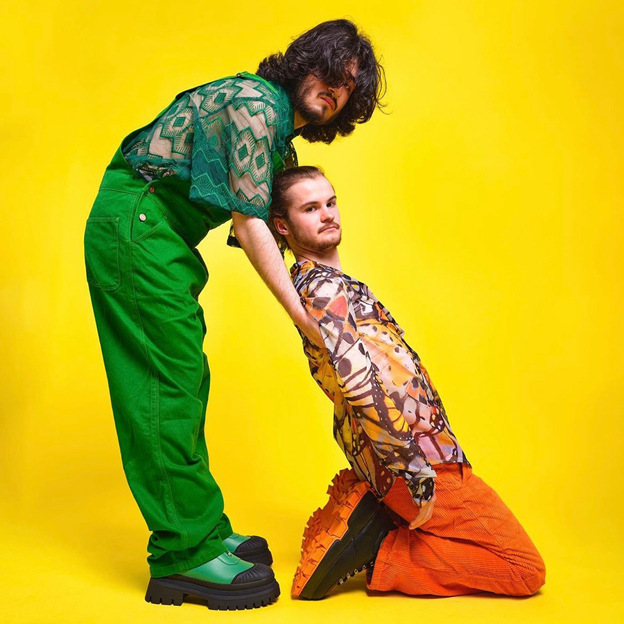 Two women in green and orange outfits against a yellow backdrop representing Cardiff's creative industry.