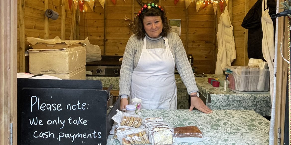 Karen Shellac stands in her Christmas stall with a chalkboard sign that states "Please note we only take cash payments"