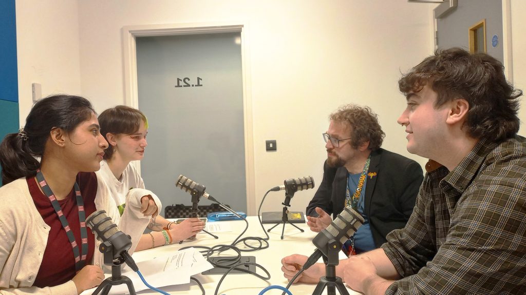 four people having a discussion by a table with four mics