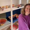 Ceramicist, Sara Moorhouse sits in front of shelves of her banded bowls