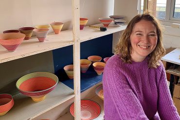 Ceramicist, Sara Moorhouse sits in front of shelves of her banded bowls
