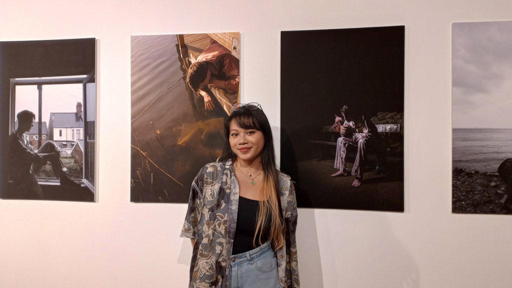 photography graduate standing in from of wall with photos