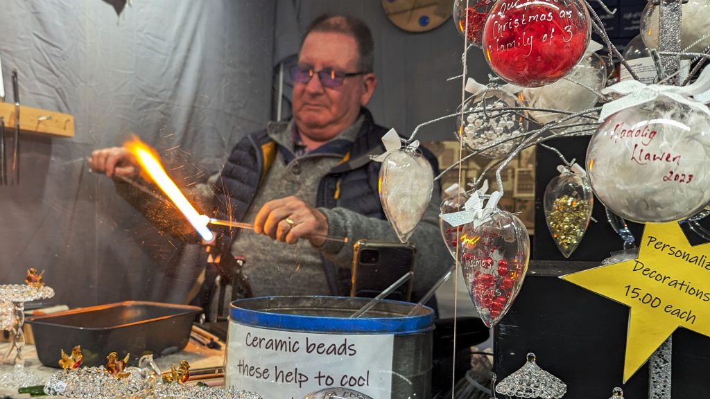 A glass artist working live on making decorations at a stall 
