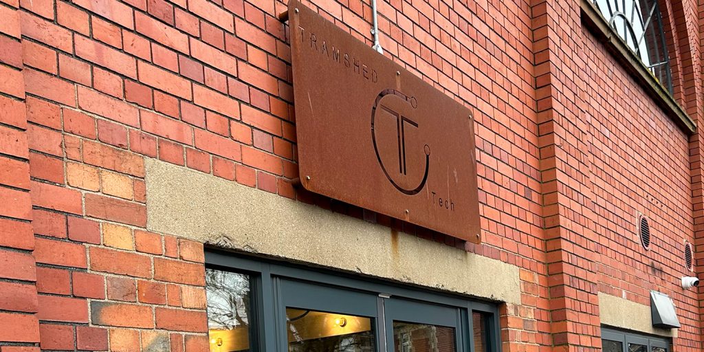 A sign reading 'Tramshed Tech' sits against a red brick wall.