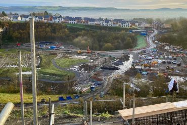 Building site with dirt tracks and forklift backed by new build homes. Construction trades in Wales suffer skills shortage.