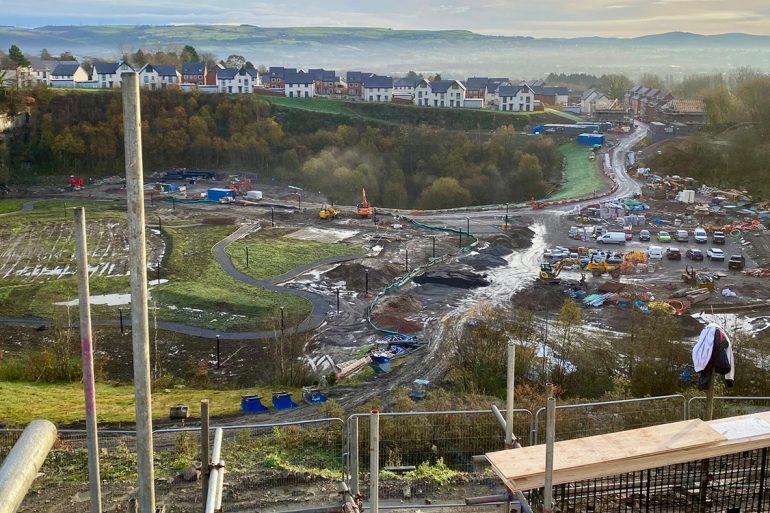 Building site with dirt tracks and forklift backed by new build homes. Construction trades in Wales suffer skills shortage.