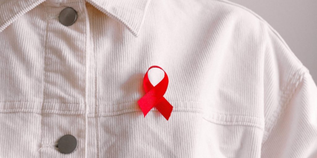 an HIV red ribbon is worn on a qhite shirt 