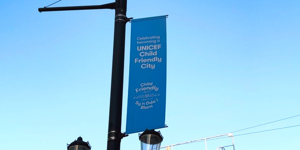 A blue banner is pictured hanging off of a black lampost