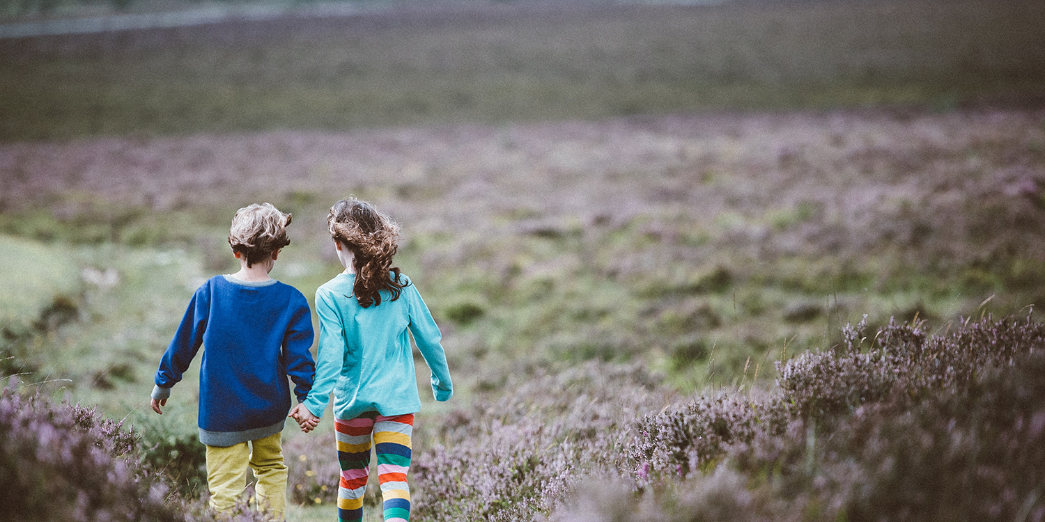 Two children walk together through grassy field holding hands. Image credit: Unsplash