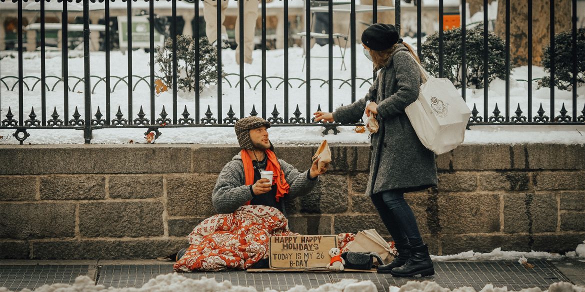 A woman handing over a sandwich to a man on the streets in winter