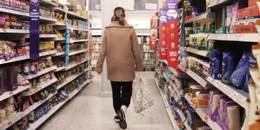 Women walking down supermarket aisle holding shopping bag in Wales.