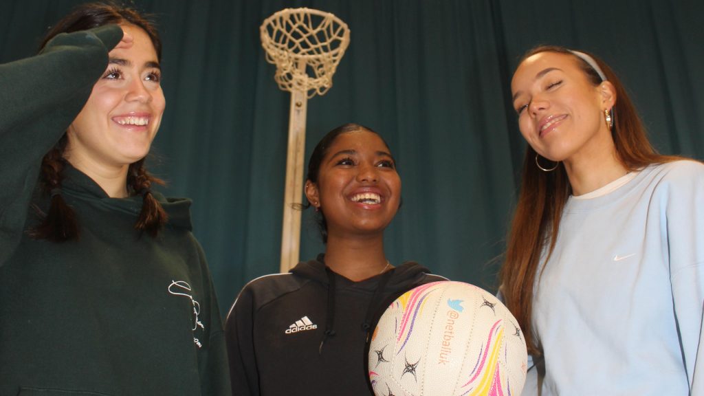 Three women laughing and playing netball together