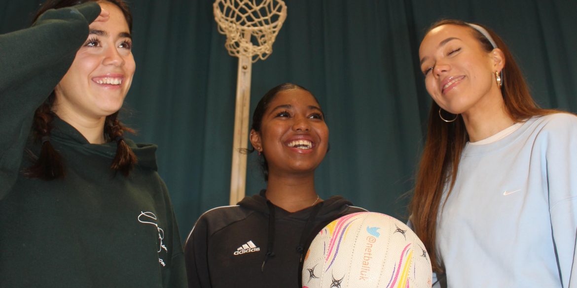 Three girls playing netball, laughing and smiling