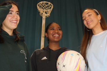 Three girls playing netball, laughing and smiling