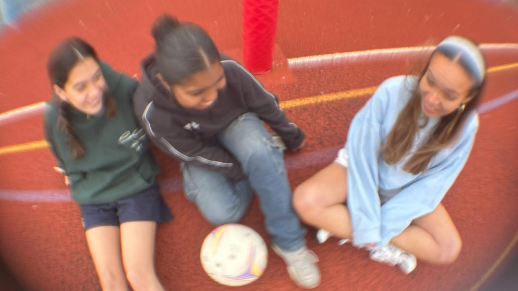 Three women laughing and playing netball together