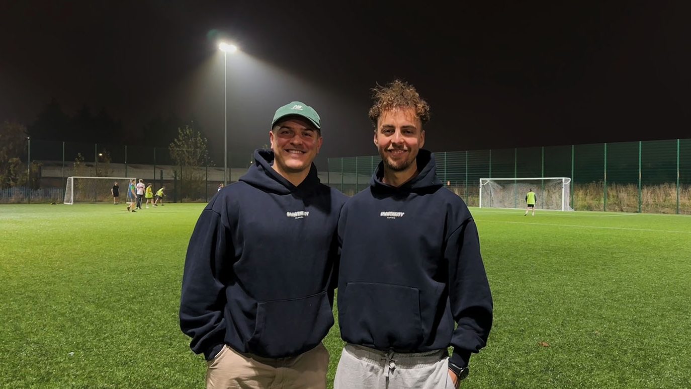 Mentality Football founders who focus on improving men's mental health in sports stand next to each other on a football pitch smiling.