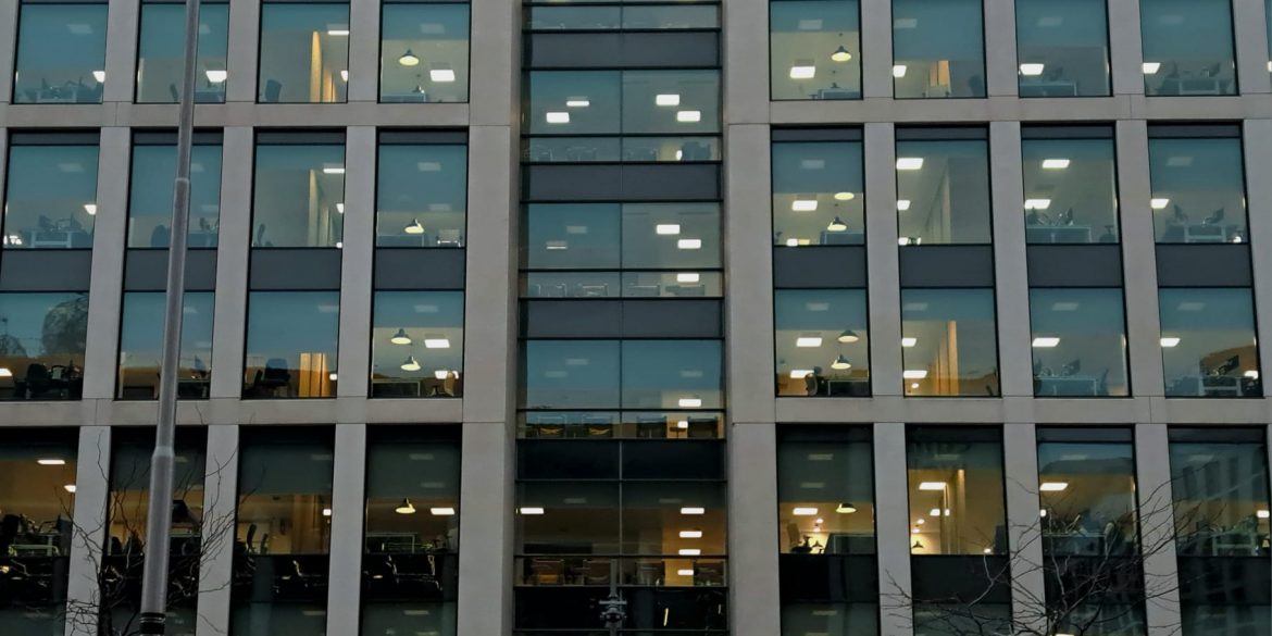 A large office with windows looking in at the office-workers, desks and laptops