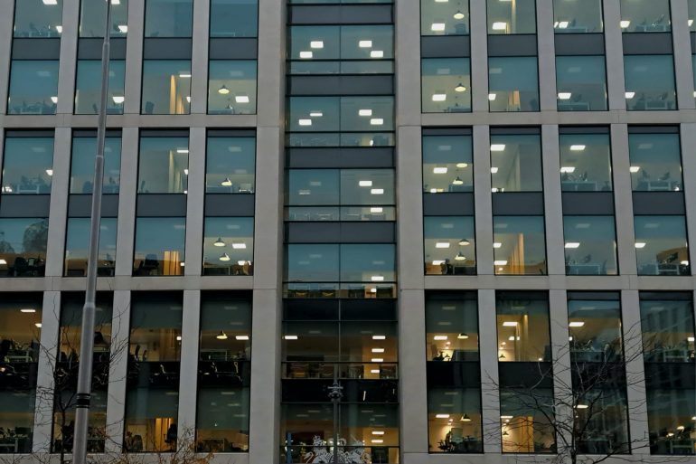 A large office with windows looking in at the office-workers, desks and laptops