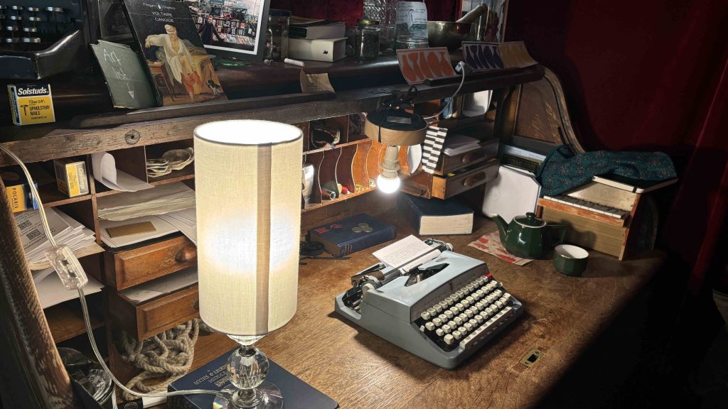 Image of Adam's writing desk which features writing materials, old bound books, and pictures of his travels