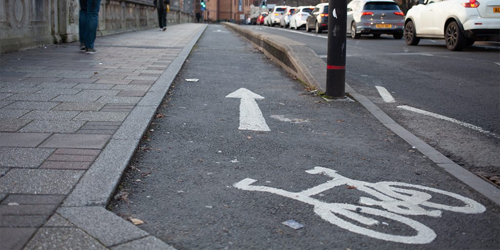 A large row of cars with a cycle path in the foreground with an arrow pointing off into the distance.