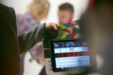 Picture of monitor on.a film set, showing actors preparing for a scene in the background