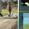 Two dog walkers walk past a bin overflowing with poo bags with an anti-dog fouling poster on the side