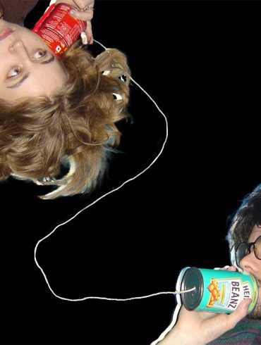 Two people talking with a can telephone, against a black background