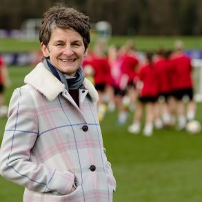 Leader in women's sports governance, Laura McAllister, in front of some female rugby players