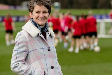 Leader in women's sports governance, Laura McAllister, in front of some female rugby players